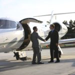 Businessmen shake hands by corporate jet